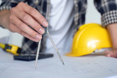 Genç Asyalı mühendis, ofisteki masanın üzerine inşaat projesi planları çiziyor..
