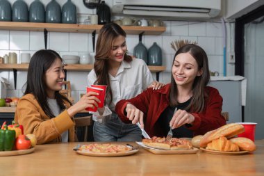 Bir grup genç bayan arkadaş masada pizza ve kırmızı içki bardaklarıyla parti veriyorlar. Konuş ve birlikte mutlu yaşa, evde eğlenmene bak...