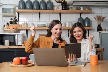 İki başarılı iş kadını ev işlerinde birlikte çalışırken sevinçlerini ifade ederler. Çevrimiçi çalışma hakkındaki fikirlerinizi paylaşın..