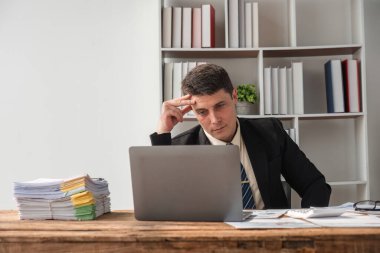 Mutsuz genç işadamı işte sıkılmış ve stresli hissediyor ofiste otururken umutsuz bir ifadeyle dizüstü bilgisayara bakıyor..