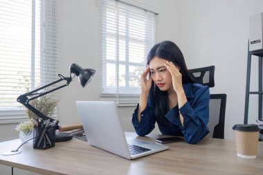 Genç Asyalı iş kadını dizüstü bilgisayar önünde online işlerini kontrol etmekte zorlanıyor. Ciddi Asyalı iş kadını bilgisayardaki iş sorunlarını çözmekten endişeleniyor.