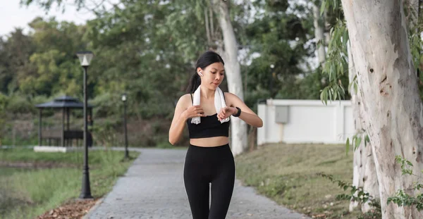 Young Asian woman uses smart watch while jogging at the park..