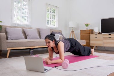 Şişman Asyalı kadın evde spor paspasının üzerinde geriniyor. Evde egzersiz yapmak, evdeki yoga minderinin üzerinde egzersiz yapmak sağlıklı ve formda kalmak için...