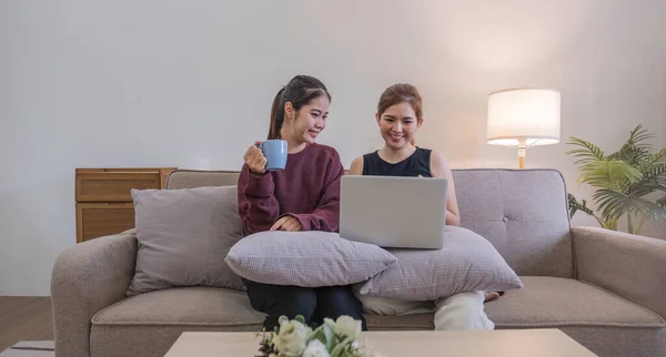 Two women communicate with friends and classmates via video link using laptop and smartphone in living room. Friends, friendship, time together..
