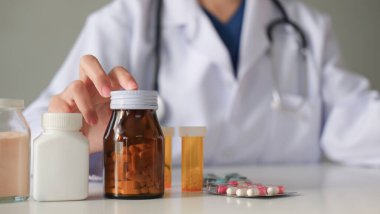 Doktor ilaç şişesini göstermek için elini kullanır ve ilaç konusunda tavsiye verir...