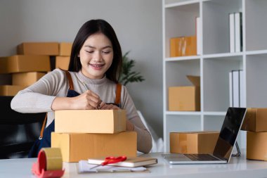 Başlangıçta KME küçük işletme girişimcisi KME ya da kutulu, çevrimiçi pazarlama paketleme kutusu ve teslimatı olan bir laptop kullanan serbest çalışan Asyalı kadın, KOBİ kavramı..