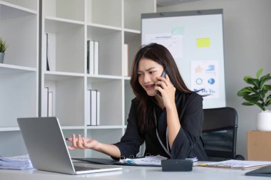 Mutlu Asyalı iş kadını modern ofiste akıllı telefon, tablet ve dizüstü bilgisayarla konuşma zevkine sahip..