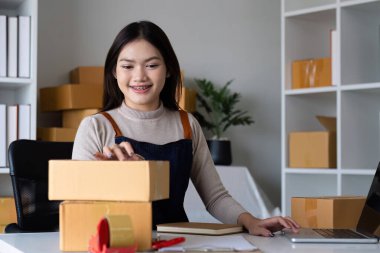 Başlangıçta KME küçük işletme girişimcisi KME ya da kutulu, çevrimiçi pazarlama paketleme kutusu ve teslimatı olan bir laptop kullanan serbest çalışan Asyalı kadın, KOBİ kavramı..