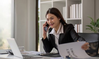 Neşeli Asyalı iş kadını modern ofiste çalışıyor. Takım elbise giyen Asyalı iş kadını şirket müdürü telefonda konuşuyor.