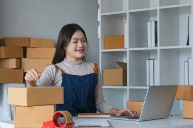 Başlangıçta KME küçük işletme girişimcisi KME ya da kutulu, çevrimiçi pazarlama paketleme kutusu ve teslimatı olan bir laptop kullanan serbest çalışan Asyalı kadın, KOBİ kavramı..