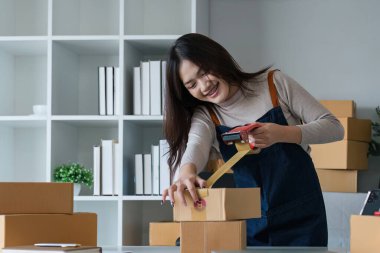 Genç Asyalı kadın, merkez ofisteki bir karton kutuyu bantlıyor. KOBİ-ticaret, yer değiştirme ve yeni küçük işletme konsepti, KOBİ kavramı..