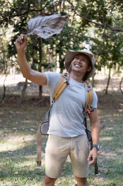 Mutlu gülümseyen Asyalı bir turistin portresi, 30-35 yaşlarında, ulusal parkta sırt çantasıyla geziyor. Asyalı erkek turist doğa aktivitelerinin, tatillerin, açık hava hobilerinin tadını çıkarıyor...