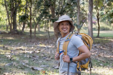 Mutlu gülümseyen Asyalı bir turistin portresi, 30-35 yaşlarında, ulusal parkta sırt çantasıyla geziyor. Asyalı erkek turist doğa aktivitelerinin, tatillerin, açık hava hobilerinin tadını çıkarıyor...
