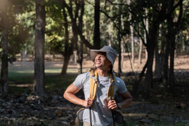 Orta yaşlı bir Asyalı turist mutlu bir şekilde gülümsedi. Ulusal parkta sırt çantasıyla gezen Asyalı erkek turist doğa aktivitelerinin tadını çıkarıyor..