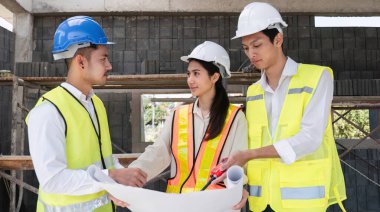 Profesyonel inşaat mühendisleri ve mimarlardan oluşan bir ekip proje planı kağıtlarını tutuyor, inşaat alanındaki inşaat projelerini denetliyor ve kontrol ediyor...