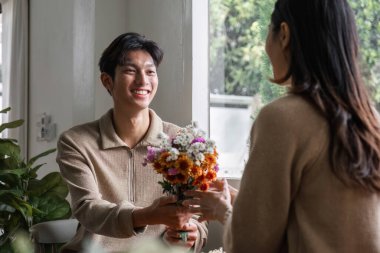 Genç bir Asyalı çift yıldönümlerinde birbirlerine çiçek verir ve birlikte oturma odasında mutlu bir şekilde otururlar...