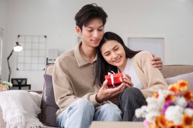 Genç bir Asyalı çift yıldönümlerinde birbirlerine hediyeler verir ve birlikte oturma odasında mutlu bir şekilde otururlar...