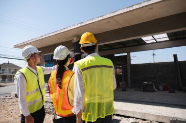 Profesyonel inşaat mühendisleri ve mimarlardan oluşan bir ekip proje planı kağıtlarını tutuyor, inşaat alanındaki inşaat projelerini denetliyor ve kontrol ediyor...