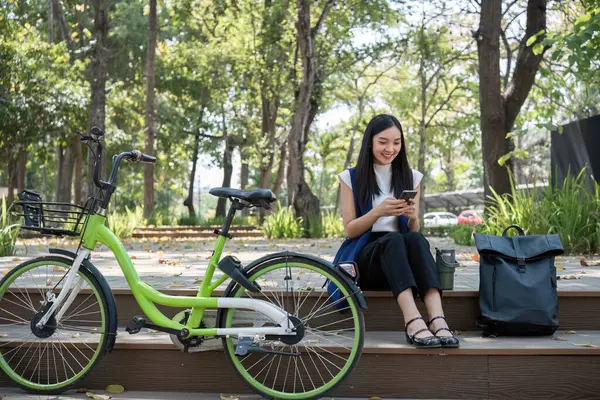 Asyalı iş kadını doğa parkında oturuyor ve çalışıyor. Çevreyi kurtarmak için bisikletle seyahat ediyor..