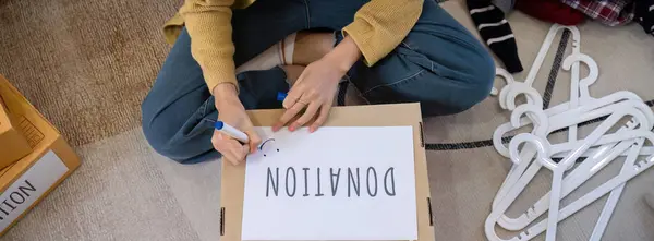 A beautiful Asian woman uses a magic marker to write on a box of clothes that will be donated to show moral support..