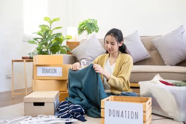 Oturma odasında kanepenin yanında oturan tatlı Asyalı kadın bağış için istenmeyen kıyafetleri sınıflandırıyor...