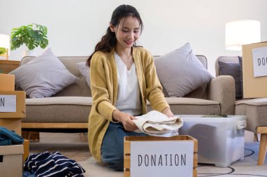 Oturma odasında kanepenin yanında oturan tatlı Asyalı kadın bağış için istenmeyen kıyafetleri sınıflandırıyor...