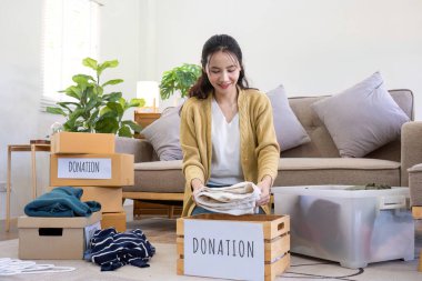 Oturma odasında kanepenin yanında oturan tatlı Asyalı kadın bağış için istenmeyen kıyafetleri sınıflandırıyor...