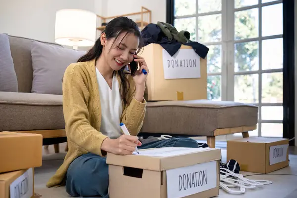 A beautiful Asian woman uses a magic marker to write on a box of clothes that will be donated to show moral support..