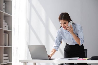 Laptop ve cep telefonu kullanan iş kadını iş ve şirket işleriyle ilgili konuşuyor..