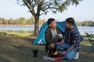 Asyalı LGBTQ çifti romantik bir kamp çadırında kahve içiyor. LGBTQ çifti kamp çadırında kahve içiyor, doğanın, ormanın, kamp ortamının, LGBTQ 'nun, gay, gay erkeklerin tadını çıkarıyor...