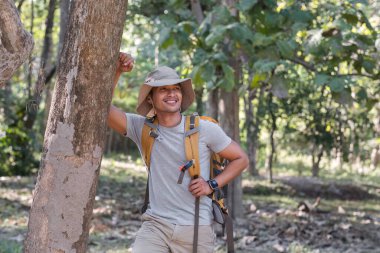 Orta yaşlı bir Asyalı turist mutlu bir şekilde gülümsedi. Ulusal parkta sırt çantasıyla gezen Asyalı erkek turist doğa aktivitelerinin tadını çıkarıyor..