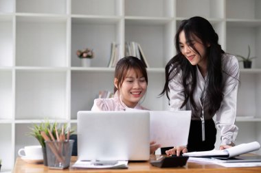 İki Asyalı iş kadını ofis masalarında iş planlama fikirlerini tartışıyor..