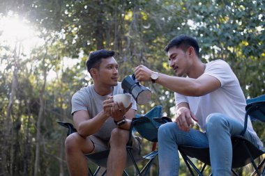 Asyalı LGBTQ çifti romantik bir kamp çadırında kahve içiyor. LGBTQ çifti kamp çadırında kahve içiyor, doğanın, ormanın, kamp ortamının, LGBTQ 'nun, gay, gay erkeklerin tadını çıkarıyor...