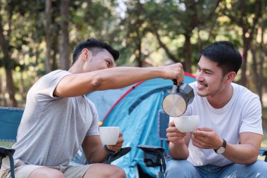 Asyalı LGBTQ çifti romantik bir kamp çadırında kahve içiyor. LGBTQ çifti kamp çadırında kahve içiyor, doğanın, ormanın, kamp ortamının, LGBTQ 'nun, gay, gay erkeklerin tadını çıkarıyor...