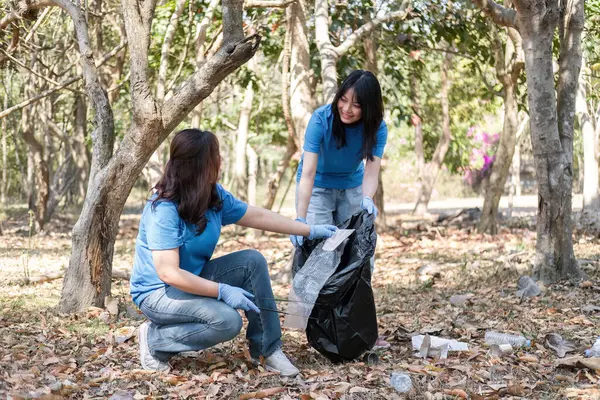 stock image A group of Asian volunteers collects trash in plastic bags and cleaning areas in the forest to preserve the natural ecosystem..