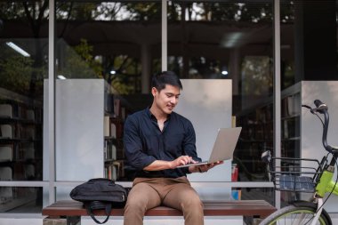 Genç bir Asyalı işadamı işe bisikletle gidiyor. Ofisin dışında oturup dizüstü bilgisayar kullanarak çalışmak...