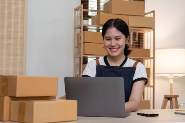 Genç bayan girişimci ürünleri çevrimiçi satmak için bir ürün kutusunun önüne yazıyor ve bunları müşterilere göndermeye hazırlanıyor. Evde satılıyor, evden çalışıyor..