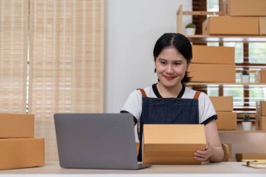Genç bayan girişimci ürünleri çevrimiçi satmak için bir ürün kutusunun önüne yazıyor ve bunları müşterilere göndermeye hazırlanıyor. Evde satılıyor, evden çalışıyor..