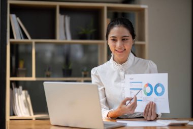 Başarılı Asyalı iş kadını otur ve rakamlarla ve grafiklerle çalış. Ofisteki masadaki dizüstü bilgisayarın üstünde..