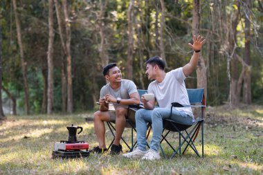Asyalı LGBTQ çifti romantik bir kamp çadırında kahve içiyor. LGBTQ çifti kamp çadırında kahve içiyor, doğanın, ormanın, kamp ortamının, LGBTQ 'nun, gay, gay erkeklerin tadını çıkarıyor...