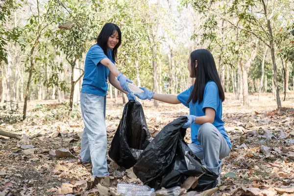 stock image A group of Asian volunteers collects trash in plastic bags and cleaning areas in the forest to preserve the natural ecosystem..