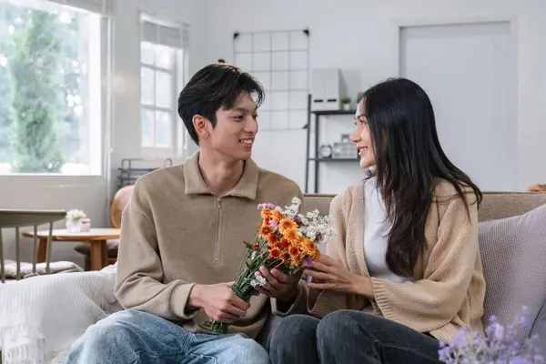 stock image Young couple hugging and showing their love to each other. And give bouquets of flowers to each other on special days or Valentines Day. On the sofa in the living room.