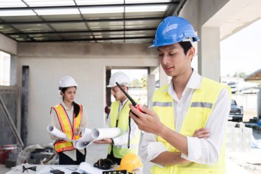 Bir elektrik mühendisi kollarını kavuşturup bir inşaat projesi planlarken elinde bir telsiz tutuyor...