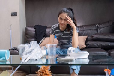 Güzel genç Asyalı kadın ev işi yaptıktan sonra yorgun ve stresli hissediyor. Oturma odasındaki kanepede ev temizleme malzemeleriyle oturuyordu...