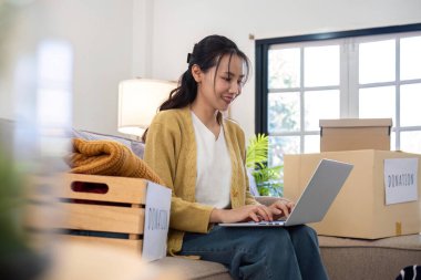 Asyalı kadın, giysi bağışı seçeneklerini araştırmak için dizüstü bilgisayar kullanıyor..