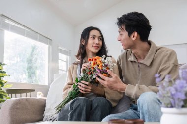 Genç çift sarılıyor ve birbirlerine sevgilerini gösteriyorlar. Özel günlerde ya da Sevgililer Günü 'nde birbirlerine çiçek buketleri verirlerdi. Oturma odasındaki kanepede..