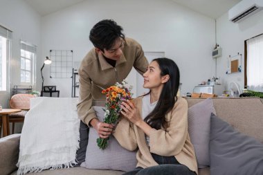 Genç çift sarılıyor ve birbirlerine sevgilerini gösteriyorlar. Özel günlerde ya da Sevgililer Günü 'nde birbirlerine çiçek buketleri verirlerdi. Oturma odasındaki kanepede..