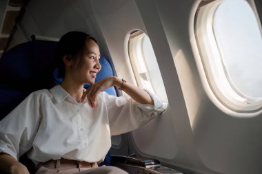 Genç Asyalı bir kadın uçuş sırasında birinci sınıf bir uçakla pencerenin yanında oturuyor. Seyahat ve iş konsepti..
