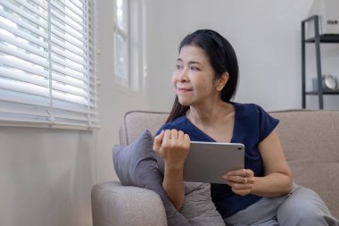 Yaşlı kadınlar boş günlerinde tabletten sosyal medya izliyor, oturma odasındaki kanepede haberleri izliyorlar..