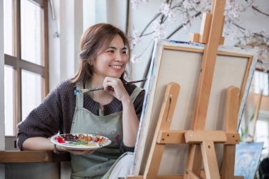 Genç Asyalı ressam elinde renkli boya paleti ile bir resim stüdyosundaki akrilik boyaları resmediyor...